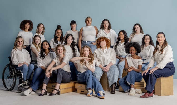 Group of women all wearing white tops and blue denim posing with blue backdrop