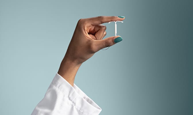 A hand holding a Mirena IUD between thumb and index fingers