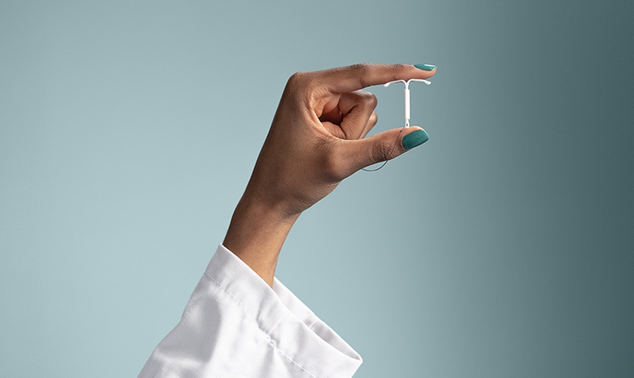 A hand holding a Mirena IUD between thumb and index fingers